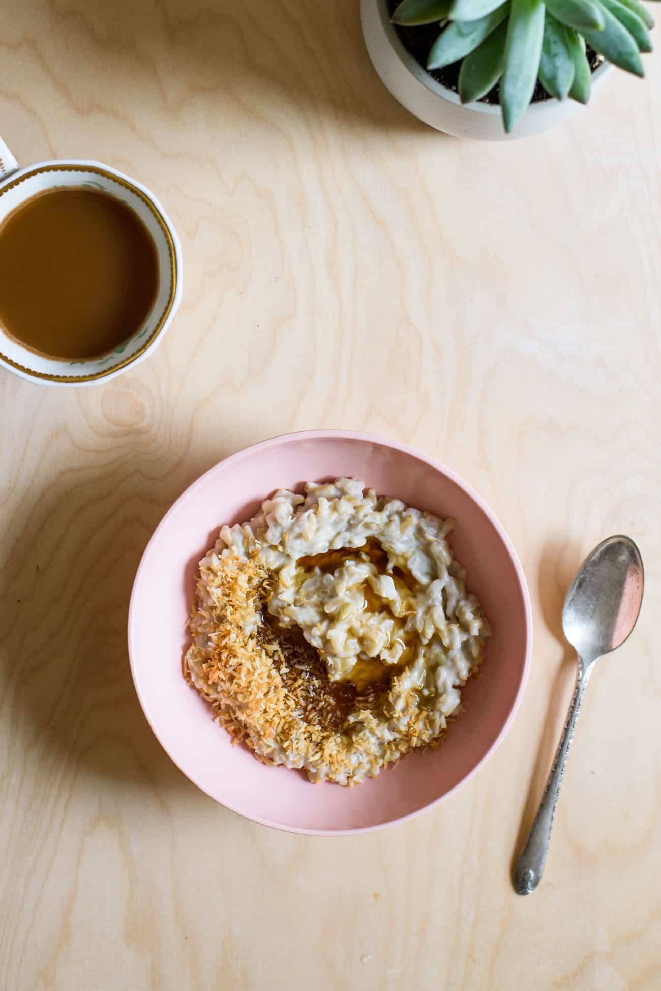 Basmati Rice Pudding with Toasted Coconut Flakes and Maple Syrup in a pink bowl next to coffee and a succulent