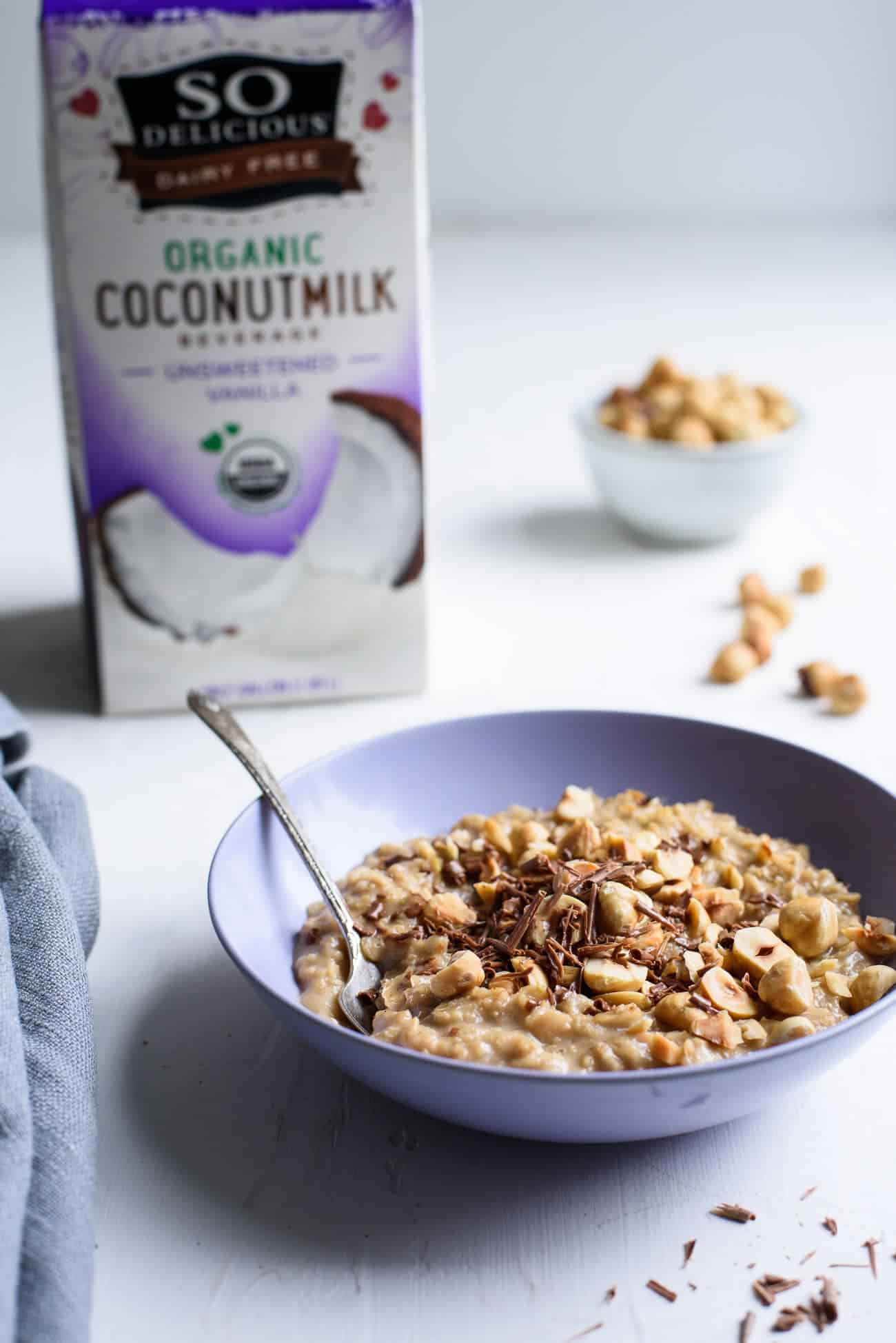 A bowl of coffee oatmeal on a white table next to a carton of So Delicious brand coconutmilk