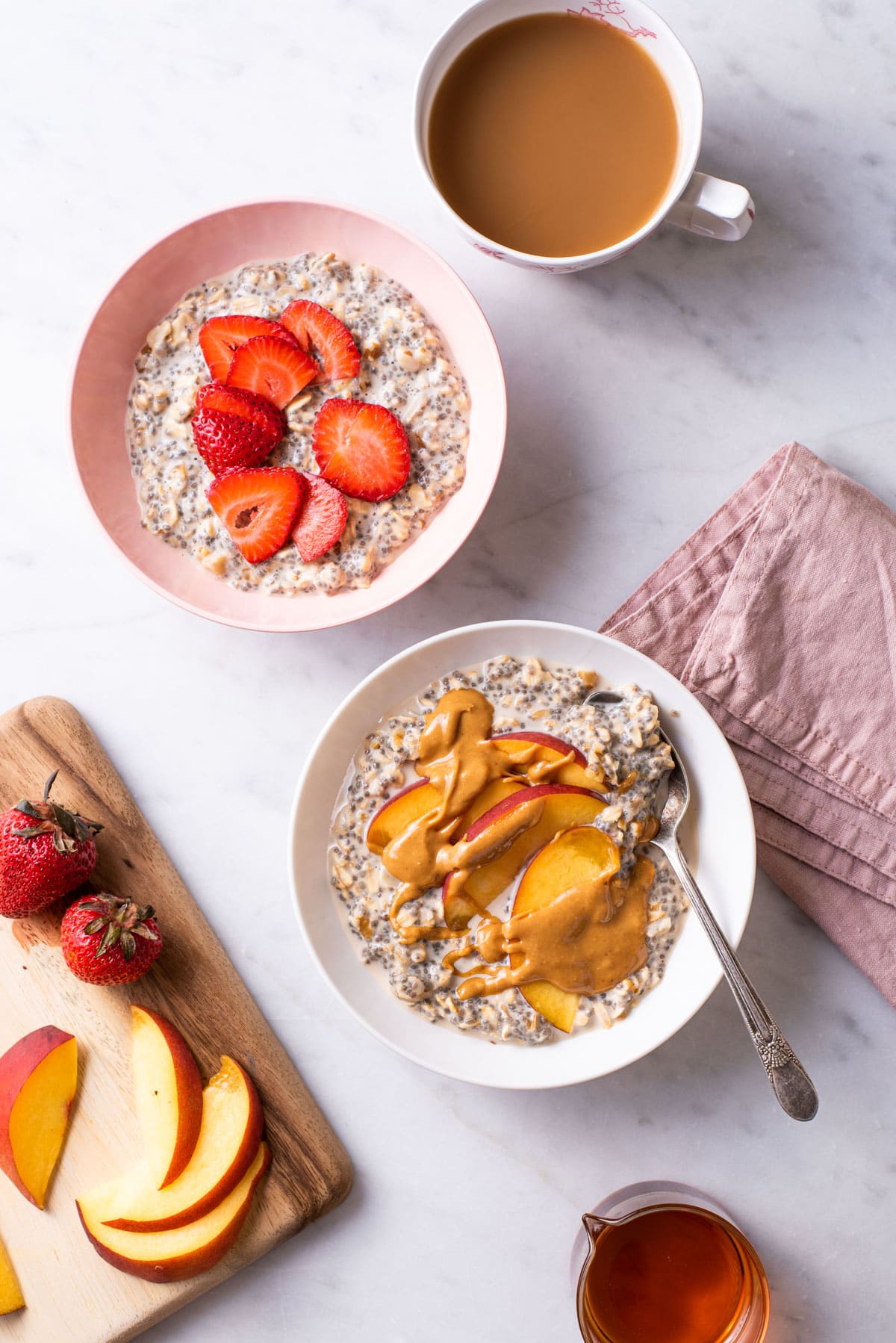 Overnight oats with chia seeds in bowls topped with fruit and nut butter, next to coffee.