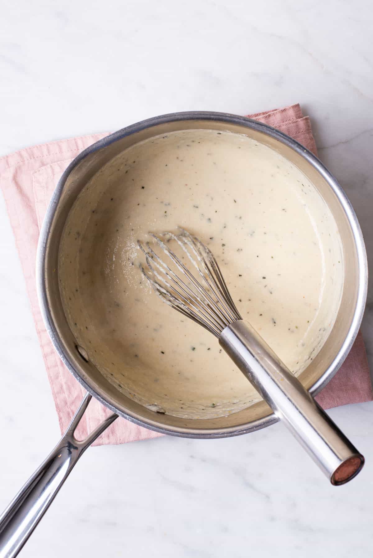 Creamy vegan cashew bechamel sauce in a pot with a whisk.