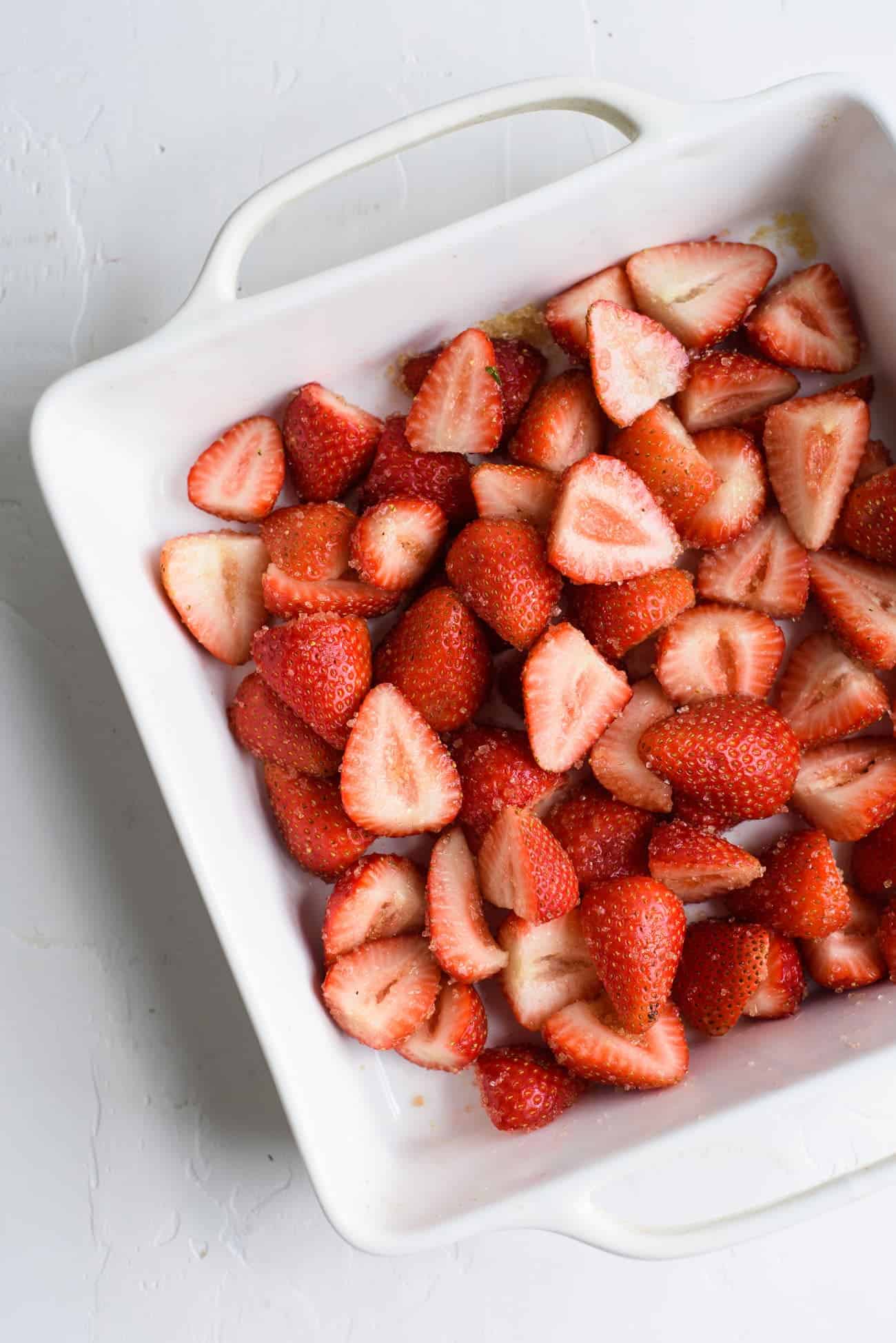 Strawberries tossed with sugar in a white baking dish, ready to be roasted