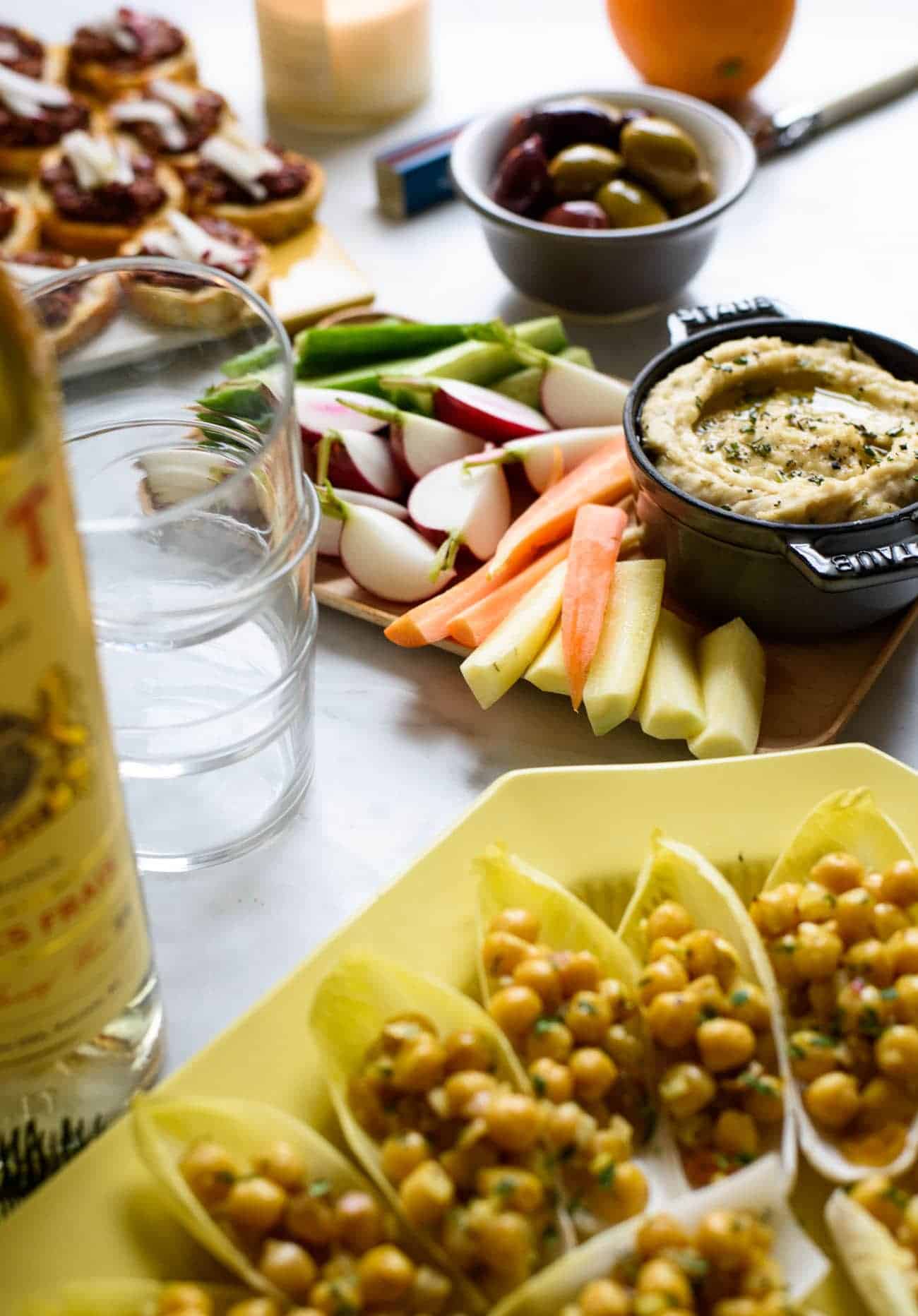 Cocktail party snacks on a marble table: white bean dip with crudites and curried chickpea salad in endive spears
