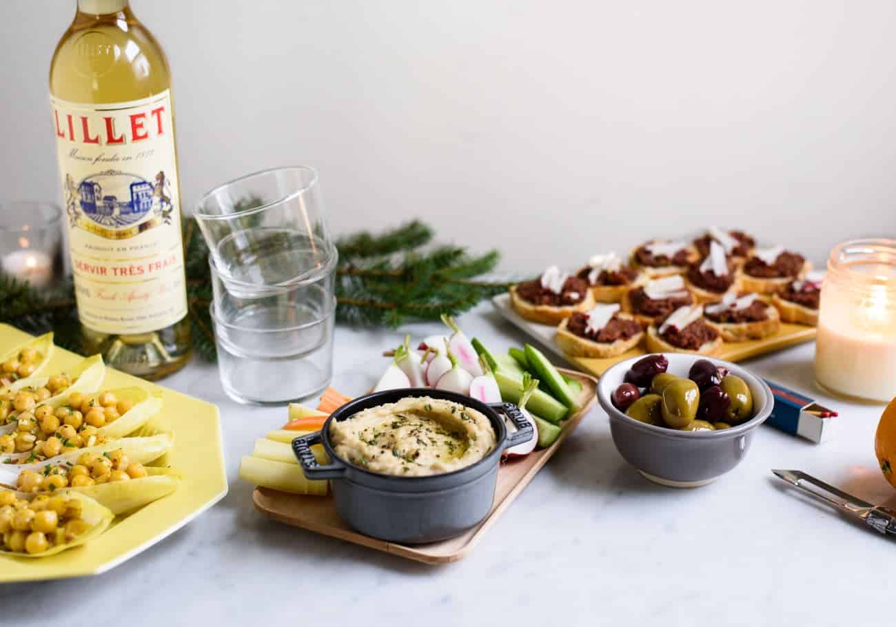 Holiday party snacks on a marble table with a bottle of Lillet Blanc