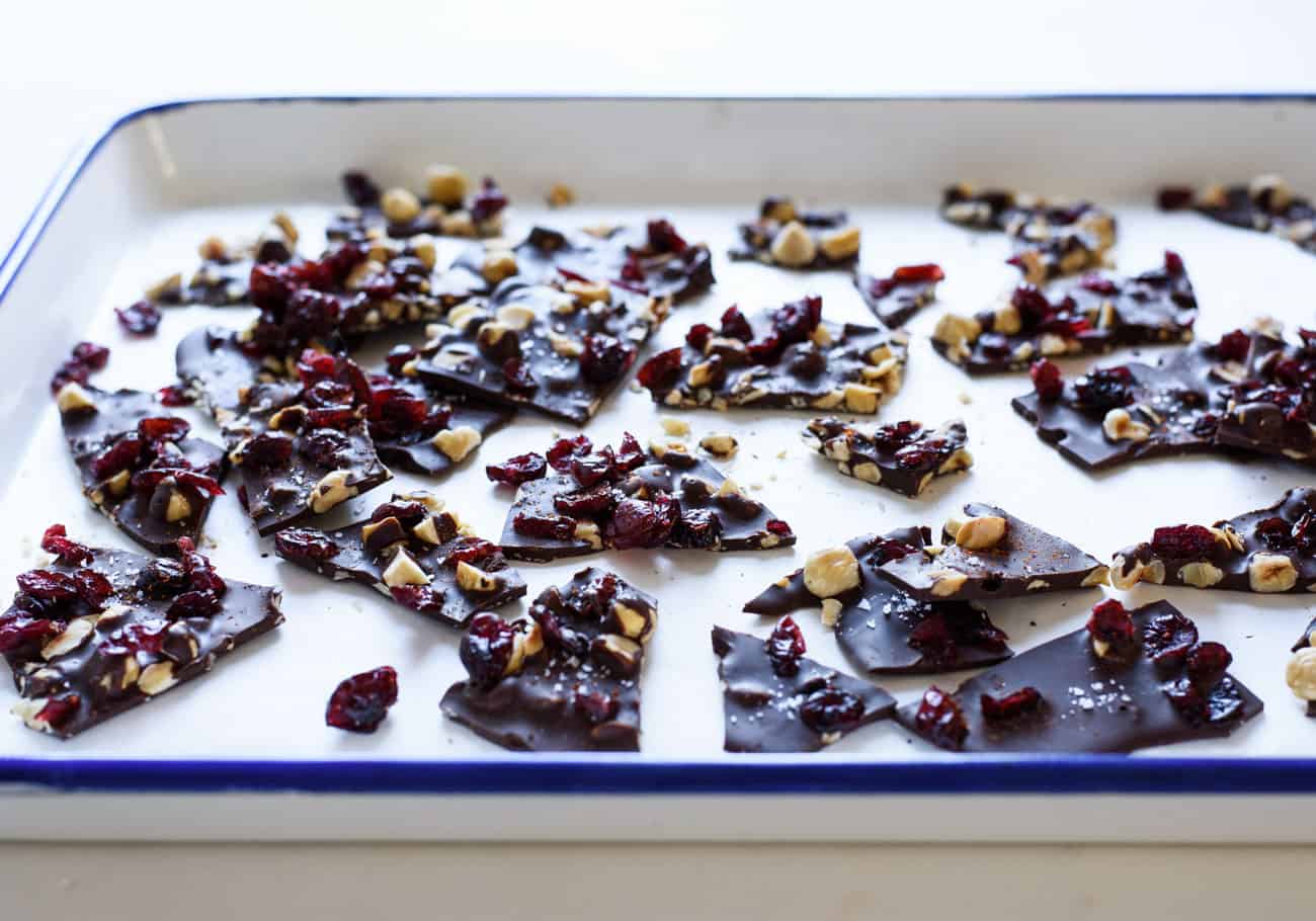 3/4-angle photo of Salted Dark Chocolate Bark with Hazelnuts, Cranberries and Cayenne Pepper on parchment paper in an enamel baking sheet