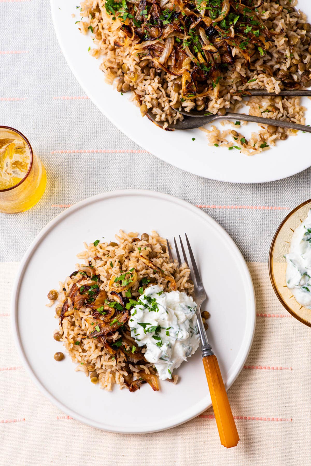 Middle Eastern Mujadara (brown rice and lentils with fried onions) on two white plates on a white table next to a yellow glass of water