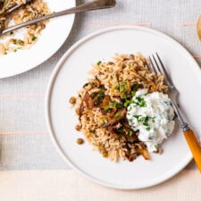 Palestinian mujadara (brown rice and lentils with fried onions) on a white plate with spiced yogurt.