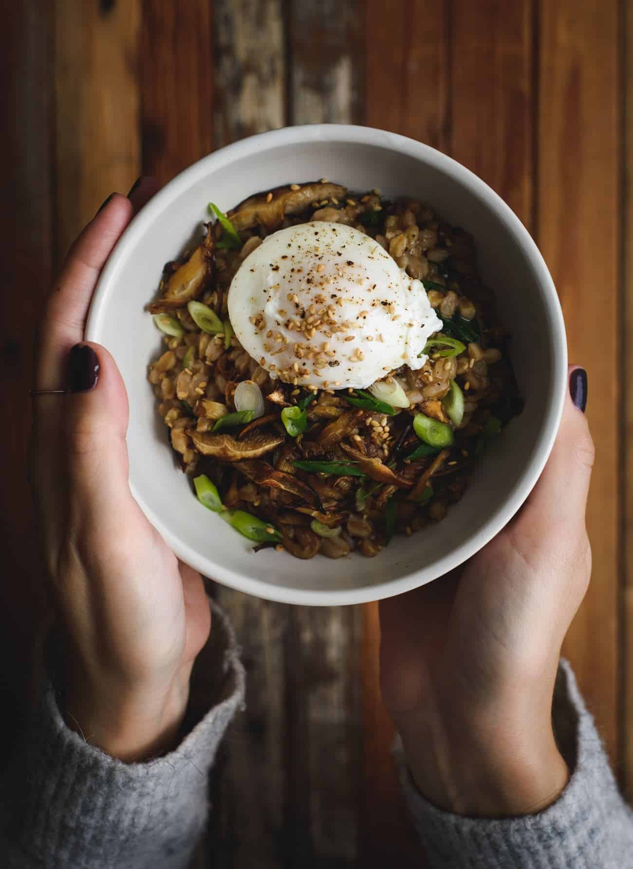 Woman's hands holding a bowl of savory porridge with a poached egg