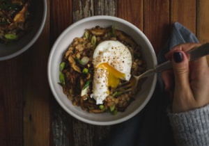 Savory farro porridge with a runny egg in a white bowl on a dark wooden background