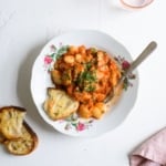 A bowl of tomato braised beans garnished with parsley with a slice of fried sourdough bread