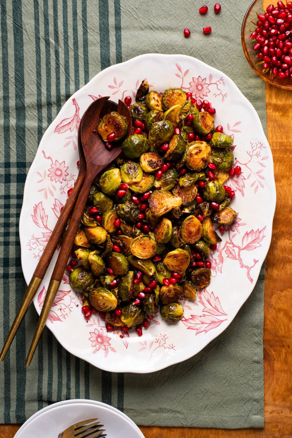 Charred Brussels sprouts with balsamic glaze and pomegranate on a vintage floral platter next to a broken pomegranate