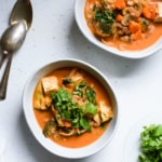 Two bowls of vegan tomato coconut curry with vegetables and tofu on a kitchen counter