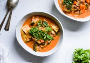 Two bowls of vegan tomato coconut curry with vegetables and tofu on a kitchen counter