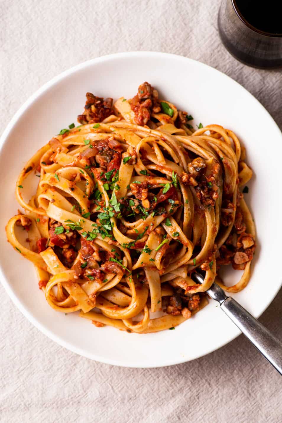 Tempeh Bolognese over spaghetti on a white plate on a wooden table