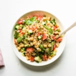 Summer farro salad in a white bowl on a white table next to a pink napkin