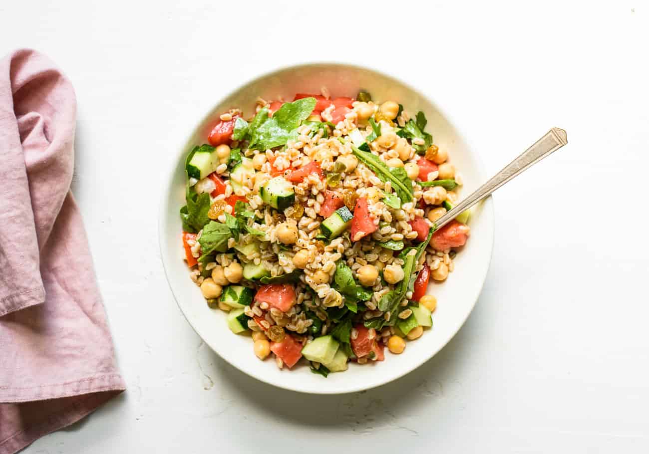 Summer farro salad in a white bowl on a white table next to a pink napkin