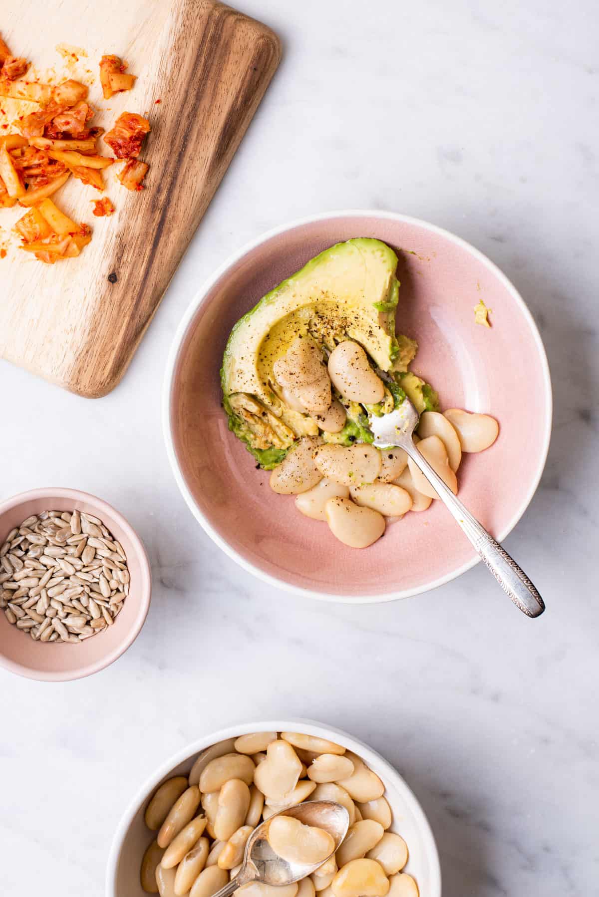 Mashing avocado with butter beans in a pink bowl.