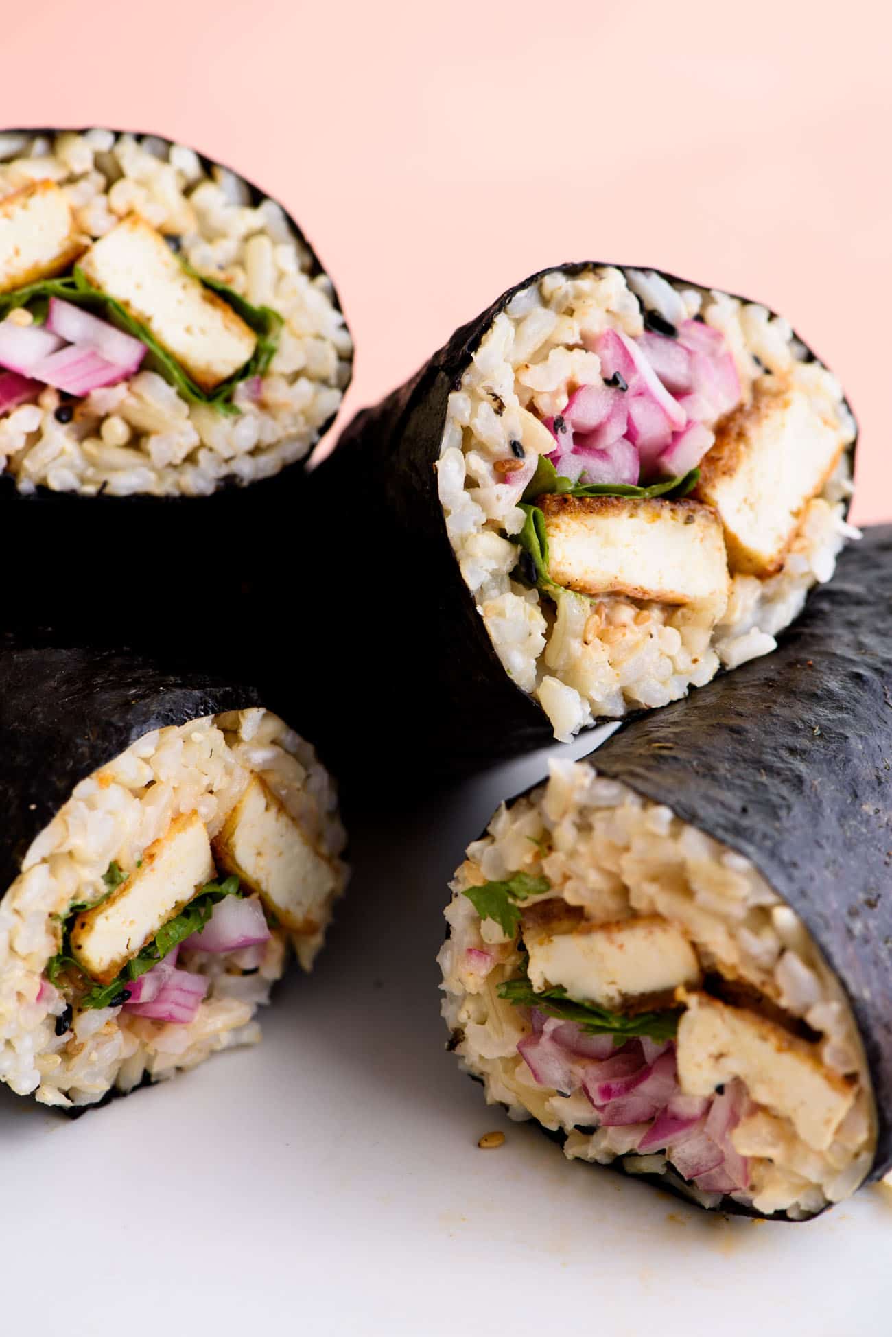 Sushi burrito halves (filled with brown rice, crispy tofu, and quick-pickled onions) stacked on a white plate