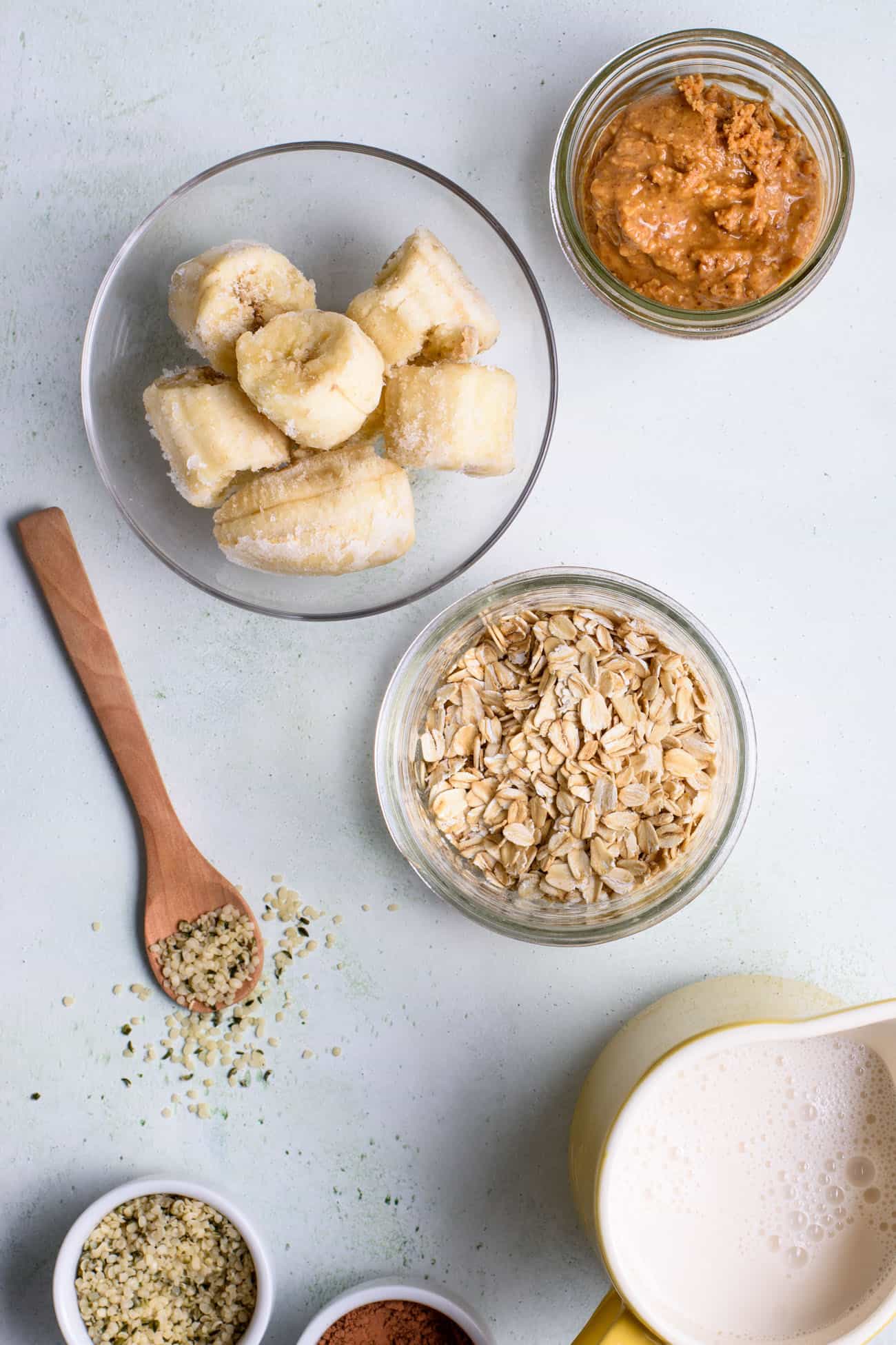 Ingredients to make a smoothie: frozen banana, oats, peanut butter, hemp seeds, almond milk, cocoa powder