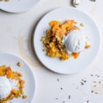 Three white plates with peach crisp with oats topped with vanilla ice cream