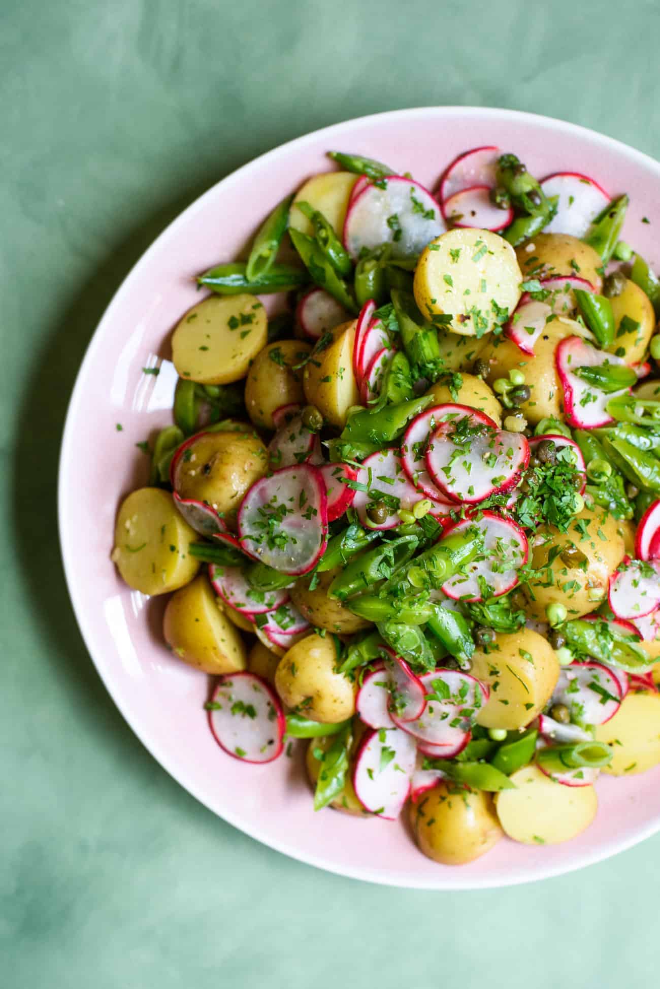 Mayo-less potato salad with radishes and sugar snap peas on a pink platter on a green table