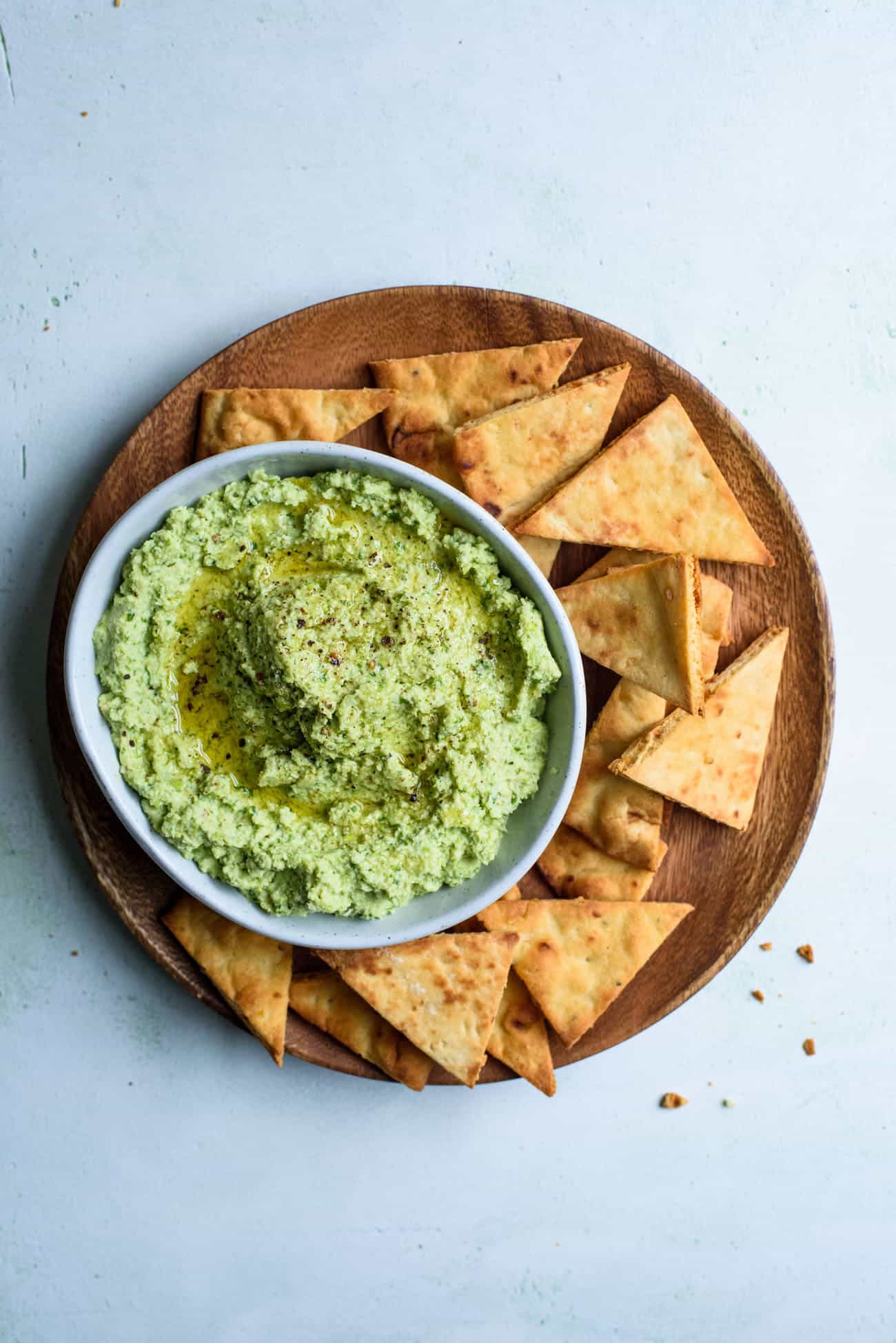 Edamame dip in a bowl on a wooden plate surrounded by pita chips