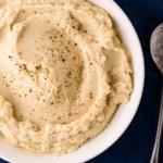Creamy celeriac puree in a white bowl on a blue tablecloth next to a metal spoon