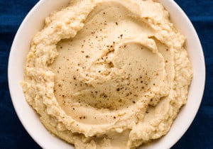 Close-up of creamy celeriac puree in a white bowl on a blue tablecloth
