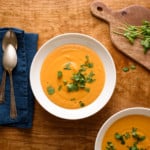 Two bowls of curried butternut squash soup with cilantro on a wooden table