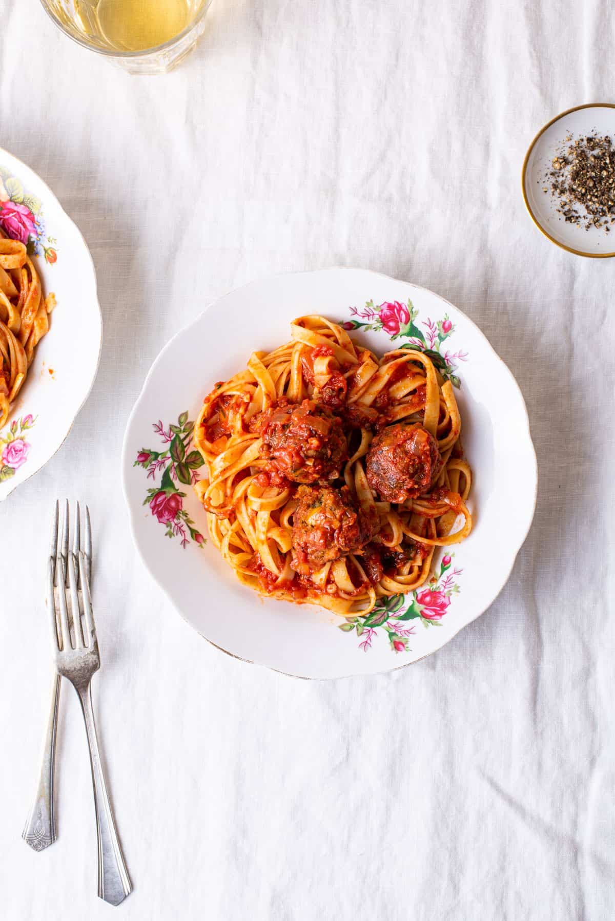 Tempeh meatballs with fettuccine and red sauce in vintage plates on a white tablecloth.