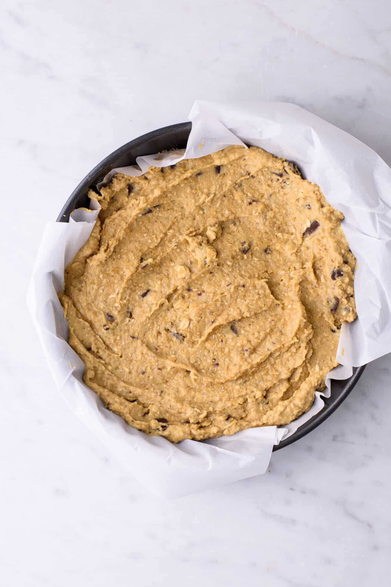Raw vegan cookie cake batter in a cake pan with parchment paper