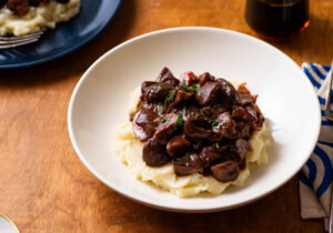 Vegan mushroom bourguignon with mashed potatoes and parsley on a black plate.