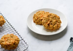 Two carrot oatmeal cookies on a white plate next to a cooling rack