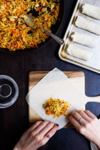 Woman's hands folding a homemade egg roll on a small wooden board