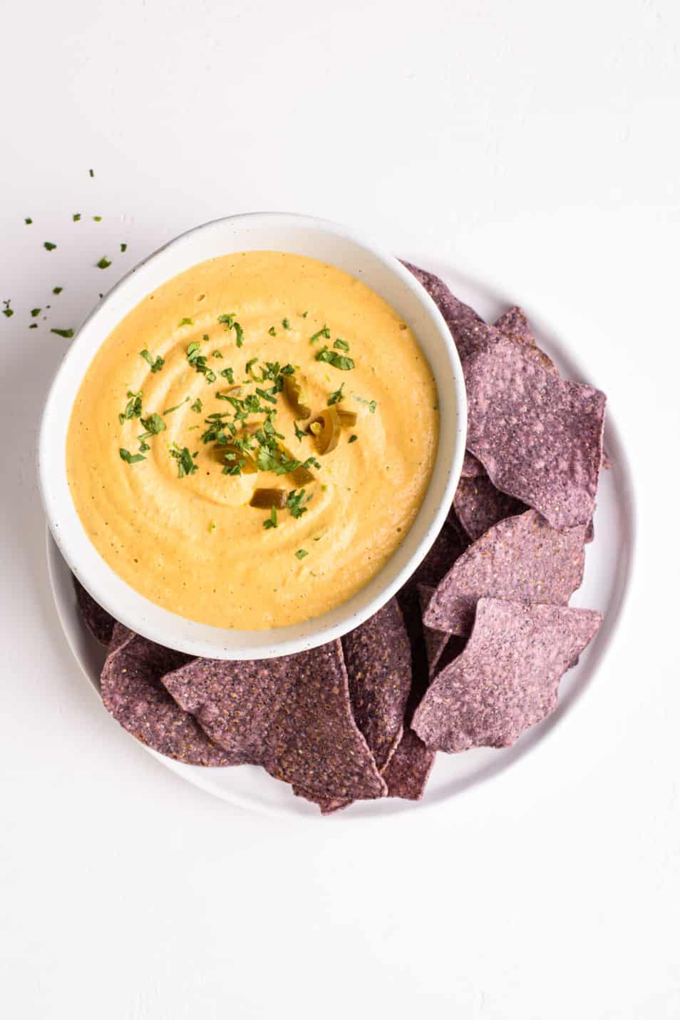 Vegan nacho cheese sauce in a bowl on a plate with blue corn tortilla chips
