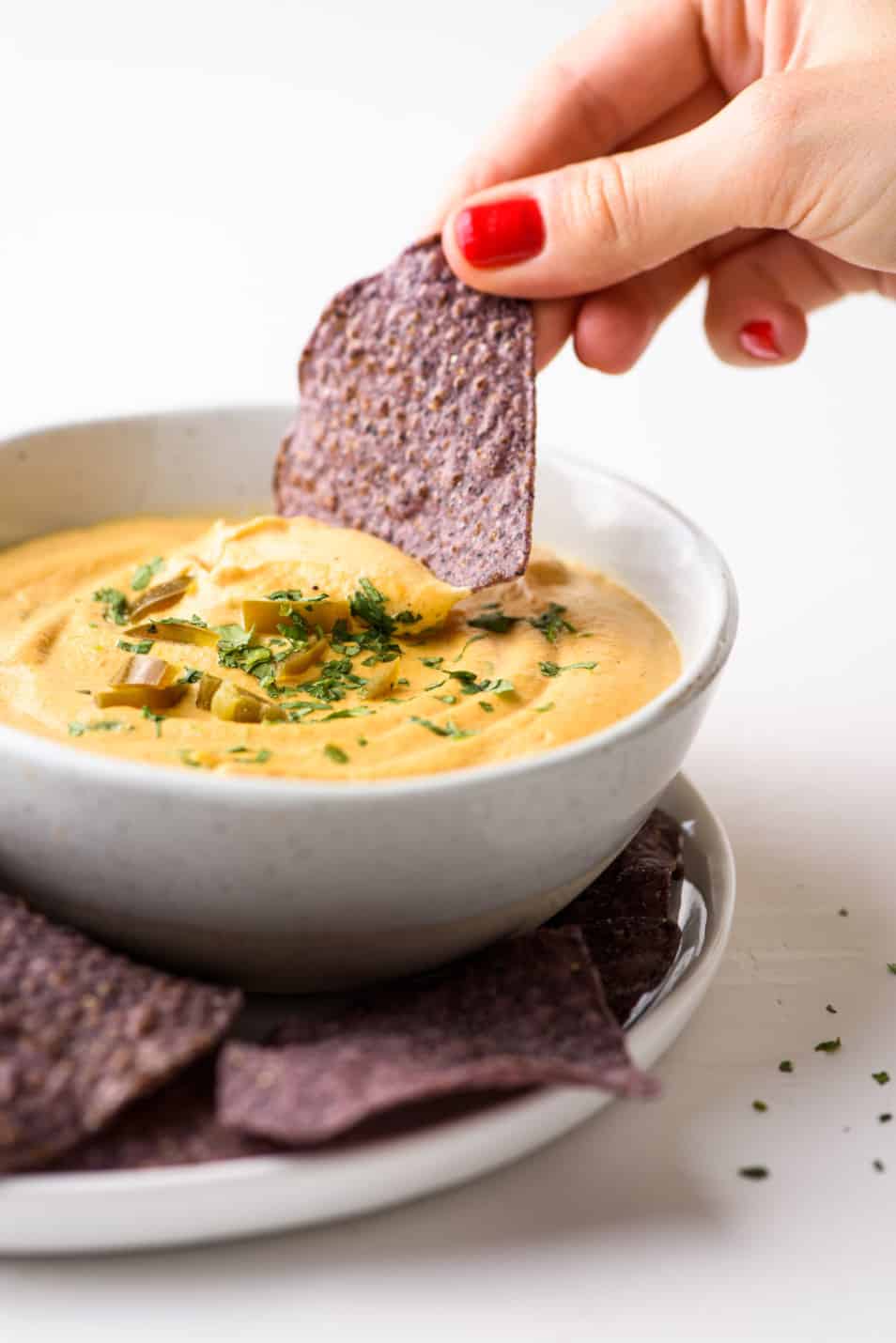 Woman's hand dipping a blue corn tortilla chip into a bowl of queso