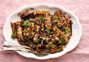 Soy-glazed pan-fried eggplant sprinkled with crushed peanuts and cilantro on a vintage oval platter on a pink tablecloth