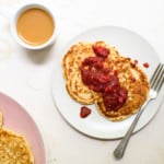 Two sourdough discard pancakes on a white plate, dolloped with strawberry chia jam, next to a cup of coffee