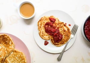 Two sourdough discard pancakes on a white plate, dolloped with strawberry chia jam, next to a cup of coffee