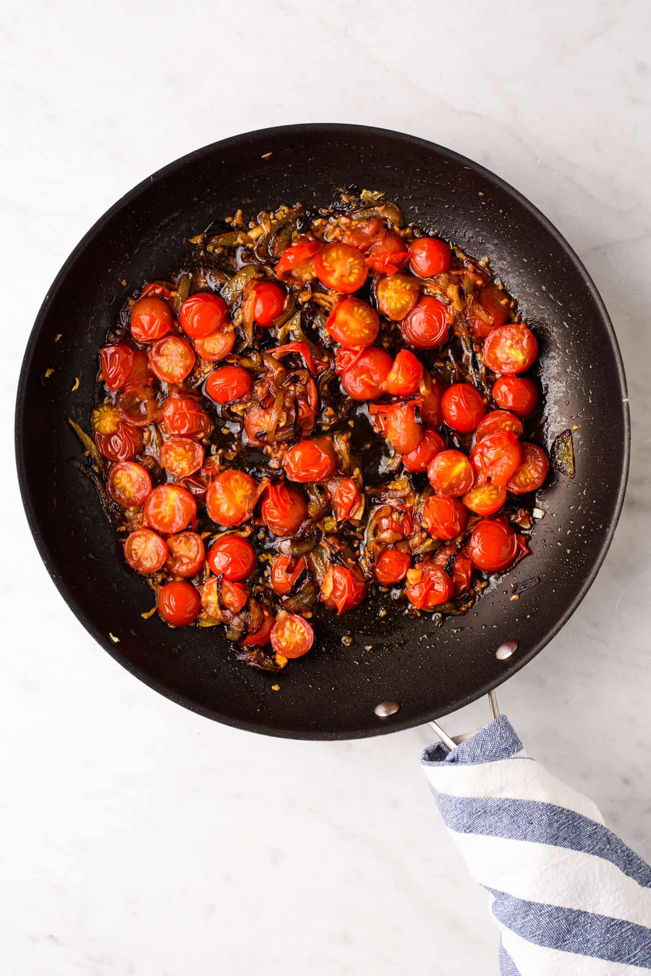 Browned onions and blistered tomatoes in a non-stick skillet on a marble table