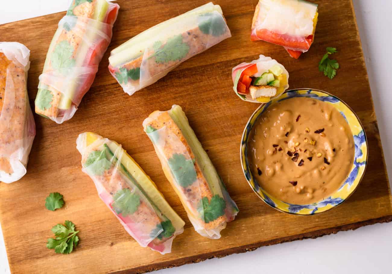 Vegan summer rolls on a wooden board next to a bowl of peanut sauce