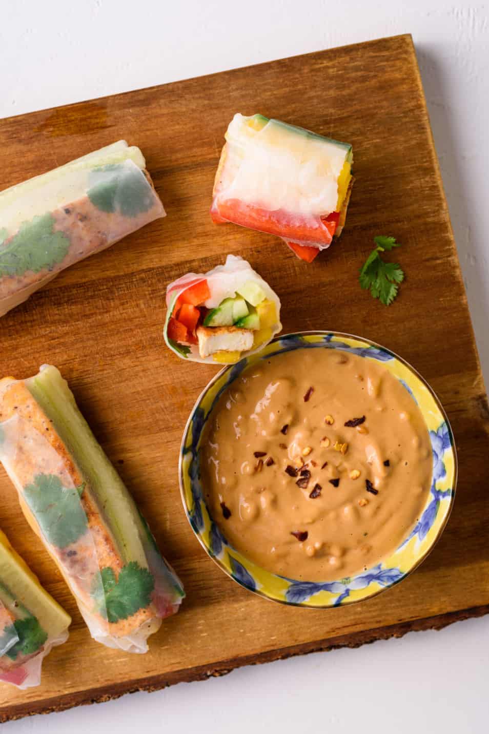 Vegan summer rolls on a wooden board next to a bowl of peanut sauce
