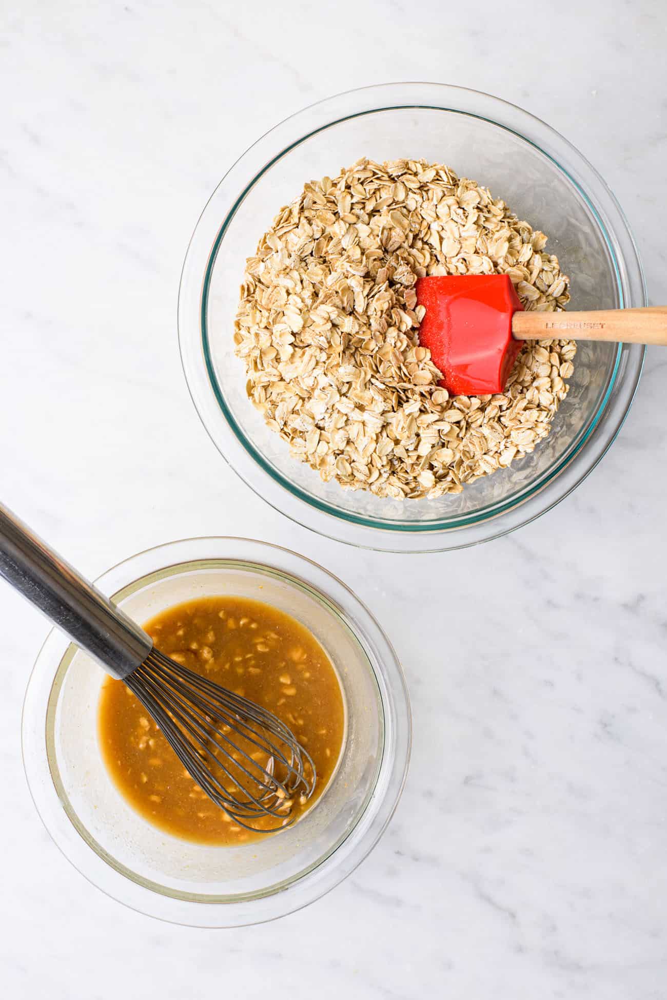 The process of making a peanut butter granola recipe: two bowls, one filled with rolled oats and the other with a mixture of peanut nutter, maple syrup, and coconut oil