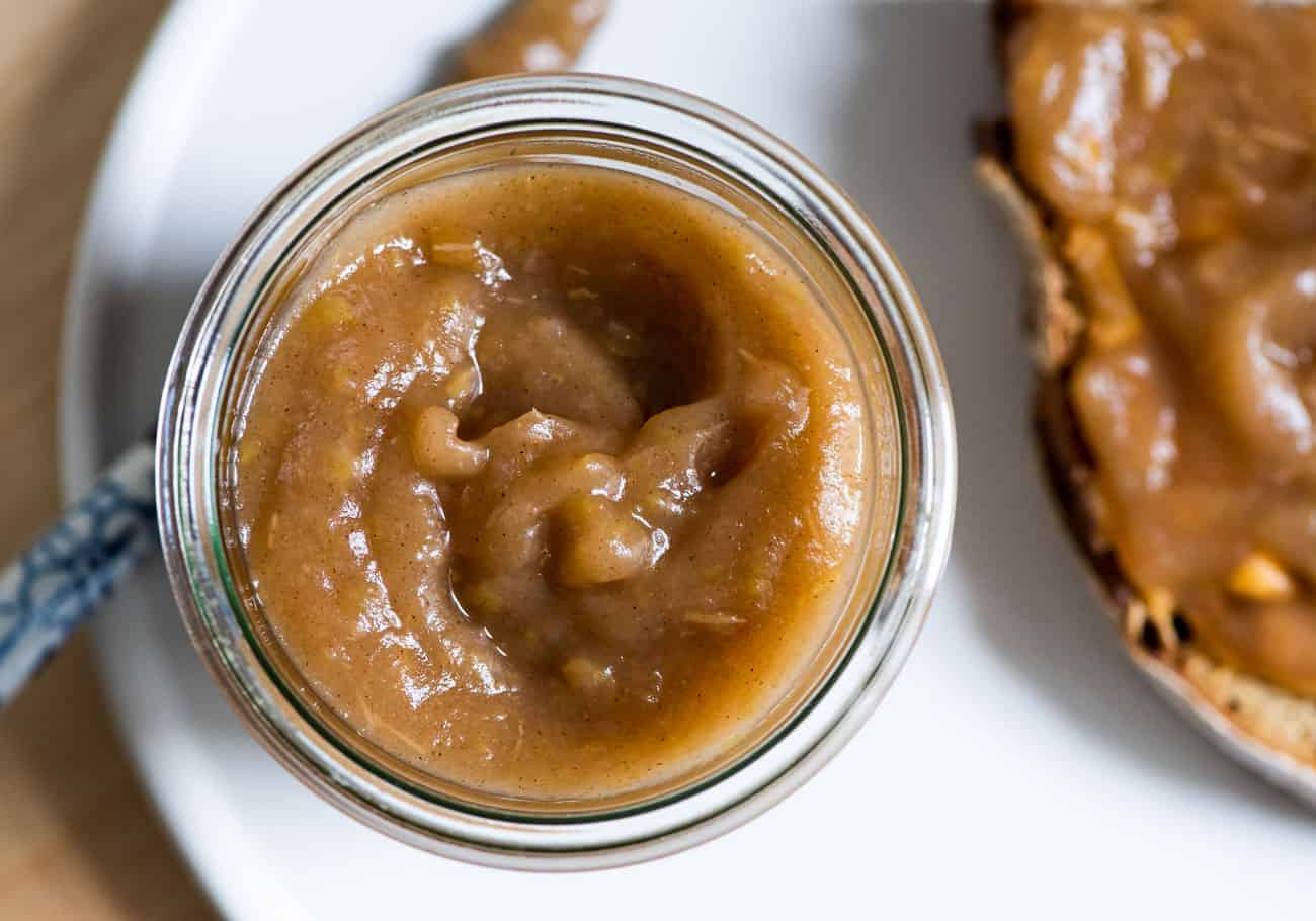 Sugar-free apple butter in a glass jar next to a piece of toast.