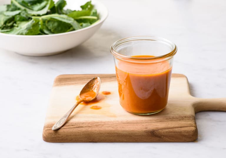 Sun-dried tomato vinaigrette in a Weck jar on a wooden board next to a bowl of greens