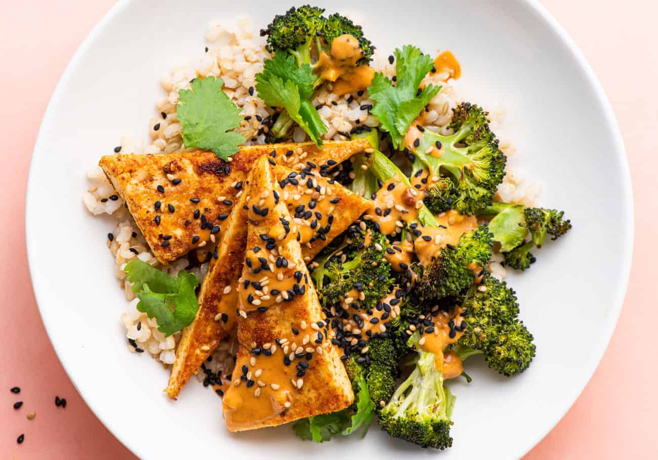 A crispy tofu bowl with brown rice, charred broccoli, and peanut sauce.