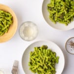 3 bowls of vegan spinach pesto pasta on a white table with white wine