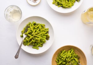 3 bowls of vegan spinach pesto pasta on a white table with white wine