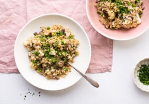 2 bowls of Vegan Mushroom Risotto with Cauliflower and Peas on a pink tablecloth, sprinkled with parsley