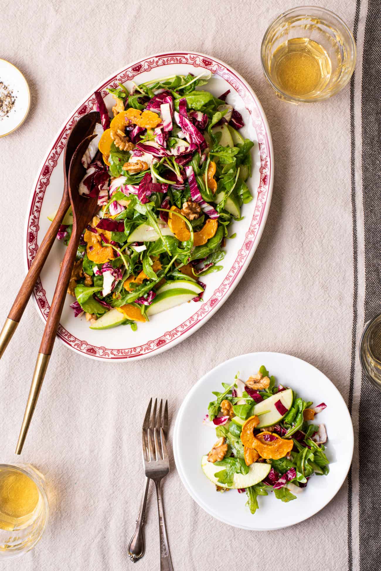 Arugula radicchio salad with delicata squash on an oval platter next to a stack of plates on a beige tablecloth