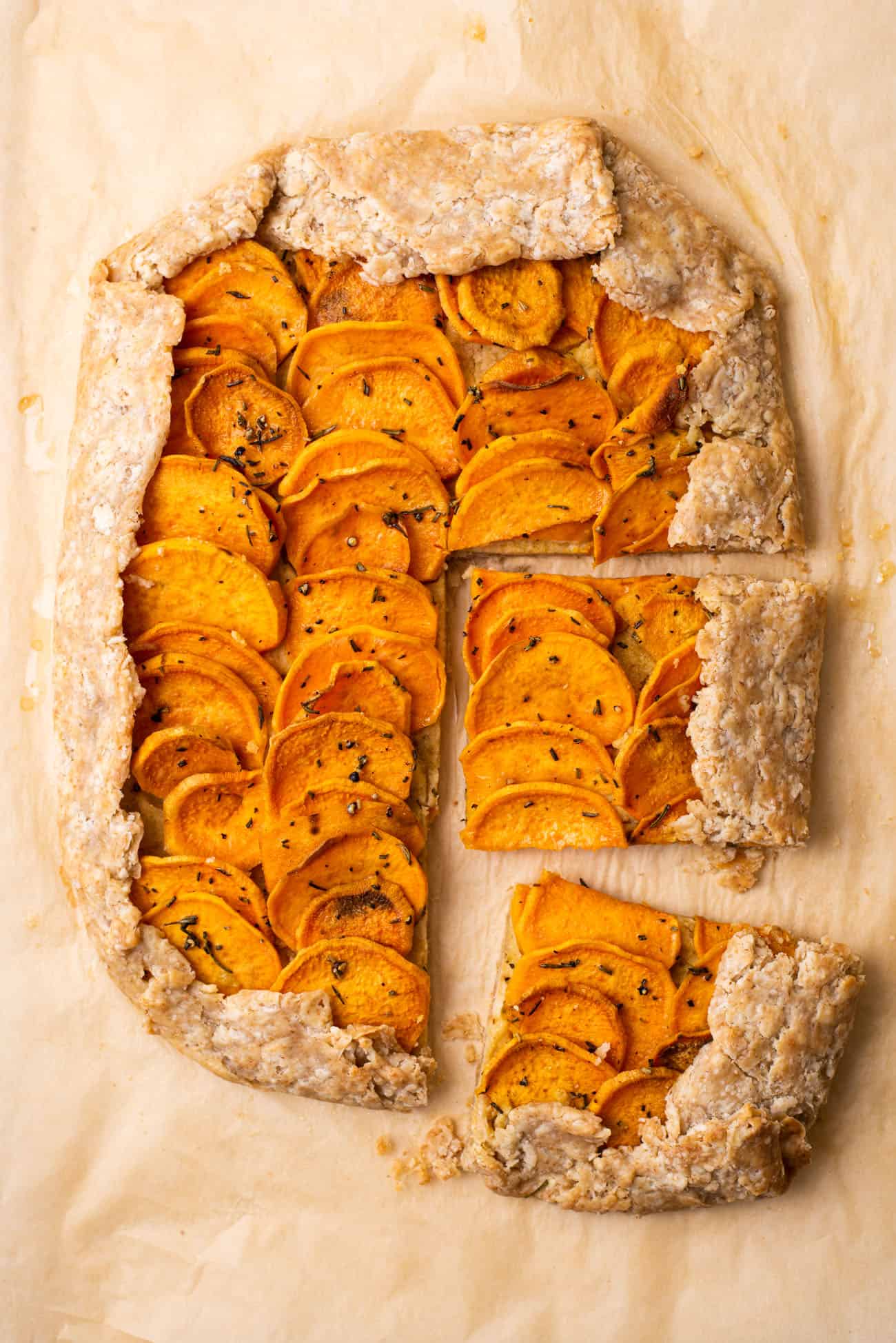Rectangular vegan sweet potato galette with cashew ricotta on brown parchment paper cut into slices.
